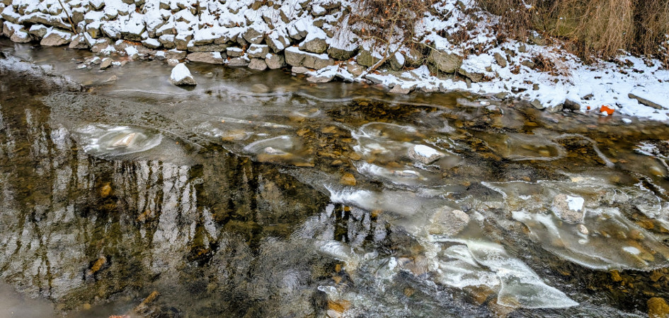 Six Mile Creek in Ithaca, NY is partially frozen with snow on the rocky far bank